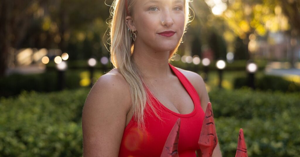 A woman in a devil costume poses with a trident during daylight, capturing the Halloween spirit outdoors.